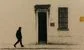 a man in a red face mask walking past a building 